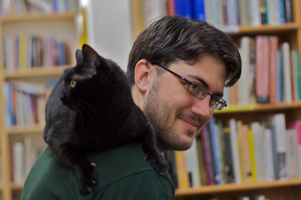 A much younger yours truly with a black cat riding on my shoulder in the aisle of a bookstore